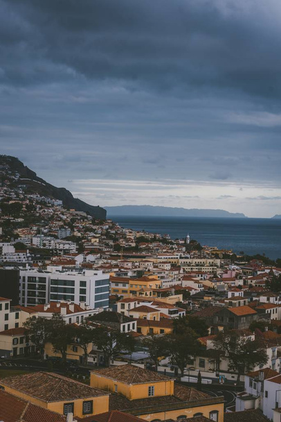 A vertical shot of buildings on the mountain under a cloudy sky in Funchal, Madeira, Portugal. - Fotó, kép