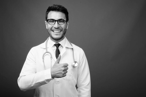 Studioaufnahme eines jungen, gut aussehenden hispanischen Arztes mit Brille vor grauem Hintergrund in schwarz-weiß - Foto, Bild