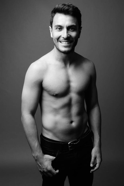 Studio shot of young handsome muscular Hispanic man shirtless against gray background in black and white - Photo, Image