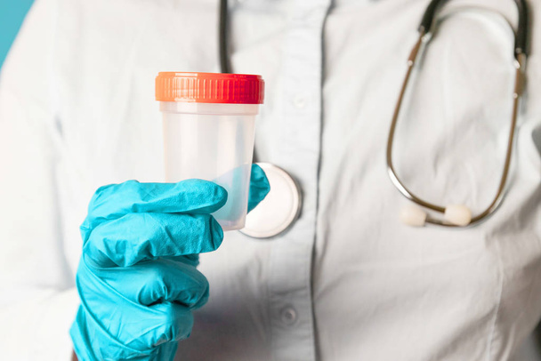 Médico mano en guante azul látex sostiene un recipiente de plástico para la prueba. Investigación del cáncer del cuerpo humano
 - Foto, imagen