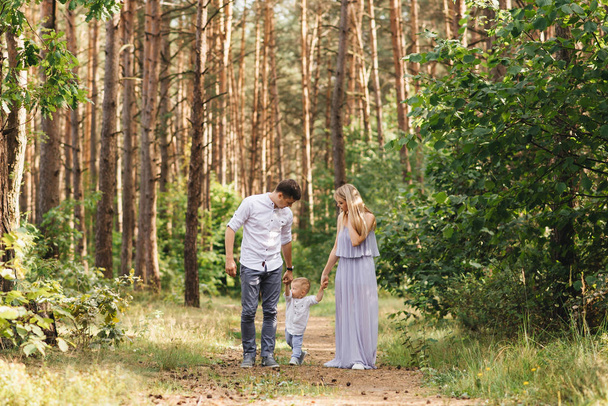 Happy young family spends time together in nature. Parents go and hold the child's hands - Φωτογραφία, εικόνα