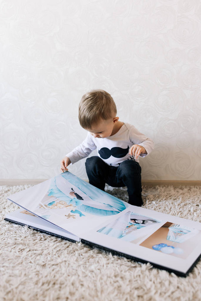 Cute baby sitting and looking at a large stylish photo book with their photos. Children's photo album - Foto, afbeelding