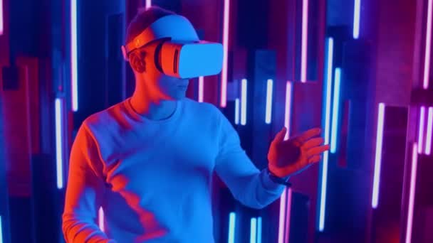Uomo con auricolare VR pendenze rapide da un lato all'altro mentre gioca nello spazio buio luce al neon illuminata
. - Filmati, video
