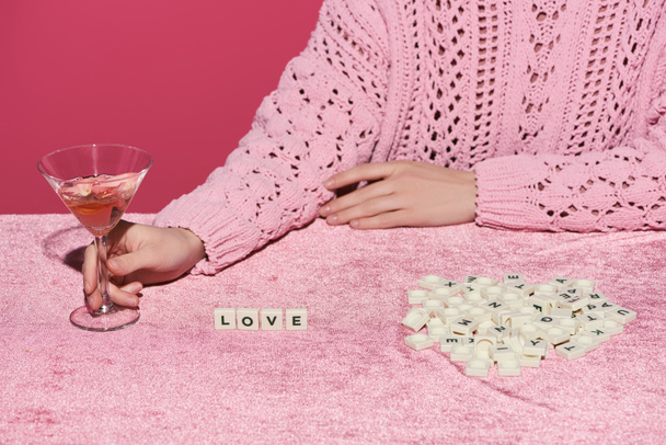bijgesneden beeld van vrouw met glas rozenwijn op fluwelen doek met liefdesbelettering op blokjes geïsoleerd op roze, meisjesachtig concept  - Foto, afbeelding