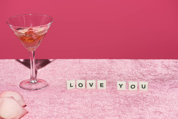 rose petals in glass near cubes with love you lettering on velour pink cloth isolated on pink, girlish concept - Photo, image