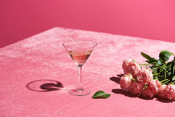 rose wine in glass near bouquet of roses on velour pink cloth isolated on pink, girlish concept - Фото, изображение