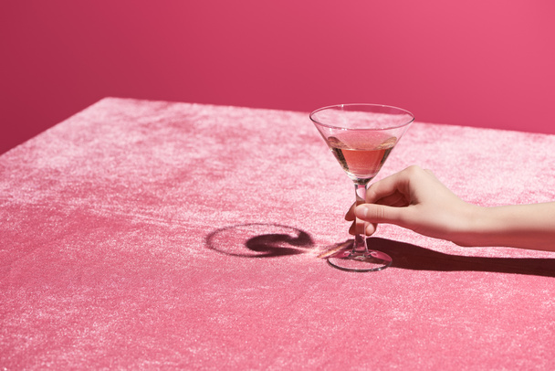 Kırpılmış bir kadın, kadife kumaş üzerinde gül şarabı bardağını tutuyor pembe, kızsı bir konseptte izole edilmiş.  - Fotoğraf, Görsel