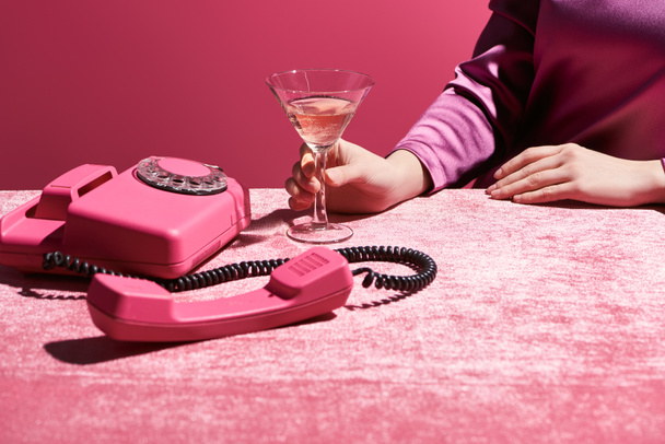 vista recortada de la mujer sosteniendo vaso de vino rosa cerca de teléfono retro en tela de terciopelo aislado en rosa, concepto femenino
  - Foto, imagen