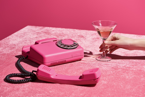 kivágott kilátás nő kezében üveg rózsa bor közelében retro telefon velúr ruha elszigetelt rózsaszín, lányos koncepció  - Fotó, kép