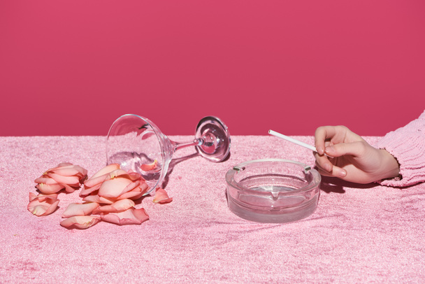 kivágott kilátás nő cigaretta és hamutartó üveg mellett rózsaszirmokkal velúr ruhán elszigetelt rózsaszín, lányos koncepció  - Fotó, kép