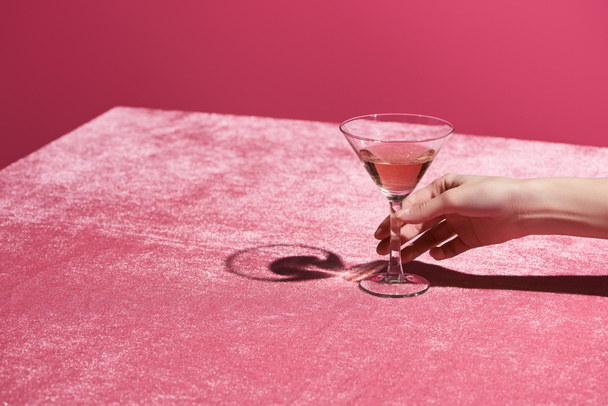 cropped view of woman holding glass with drink on velour cloth isolated on pink, girlish concept - Foto, Imagem