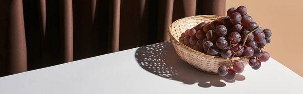bodegón clásico con uva en canasta de mimbre en la mesa cerca de la cortina aislada en beige, plano panorámico
 - Foto, imagen