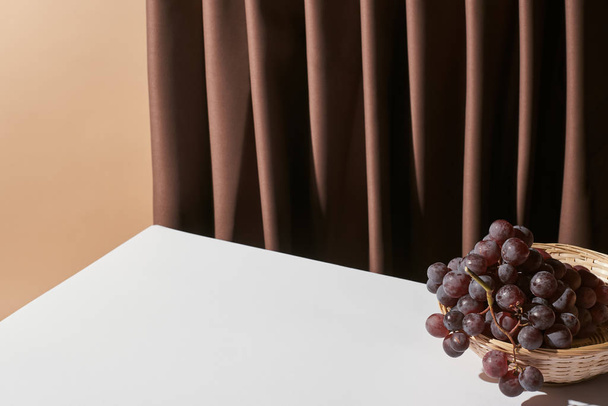 classic still life with grape in wicker basket on table near curtain isolated on beige - Valokuva, kuva