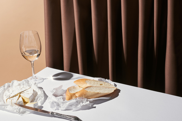 classic still life with baguette, Camembert cheese and white wine on table near curtain isolated on beige - Photo, Image