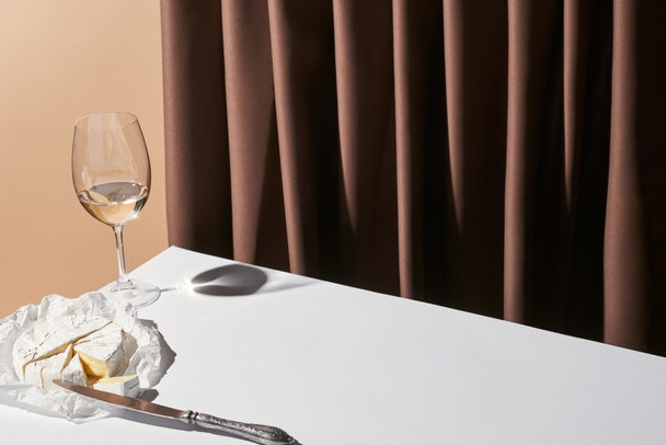 klasická zátiší se sýrem Camembert a bílým vínem na stole poblíž opony izolované na béžové - Fotografie, Obrázek