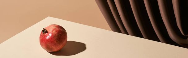 classic still life with pomegranate on table near curtain isolated on beige, panoramic shot - 写真・画像