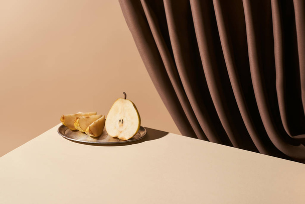 klassieke stilleven met peer op zilveren plaat op tafel in de buurt van gordijn geïsoleerd op beige - Foto, afbeelding