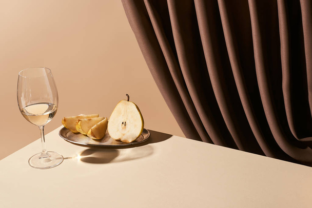bodegón clásico con pera y vino blanco en la mesa cerca de la cortina aislado en beige
 - Foto, Imagen