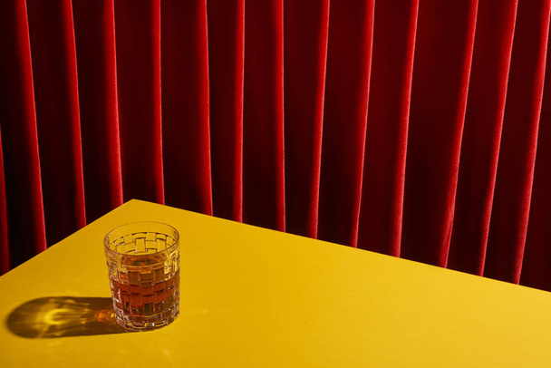 classic still life with glass of drink on yellow table near red curtain - Φωτογραφία, εικόνα