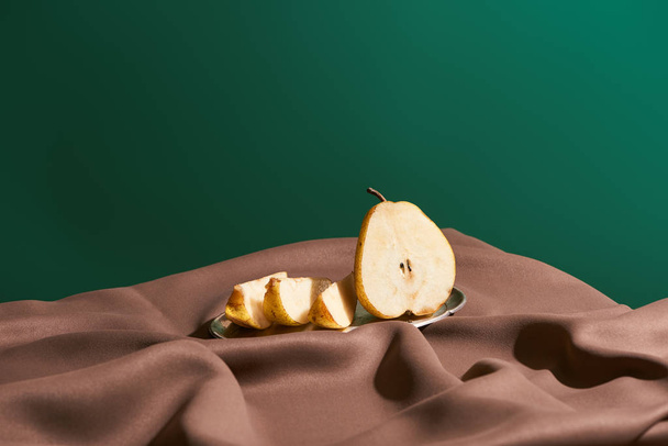 classic still life with cut pear on silver plate on table with brown tablecloth isolated on green - Photo, Image