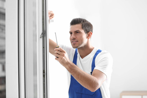 Construction worker repairing plastic window with screwdriver indoors - Zdjęcie, obraz