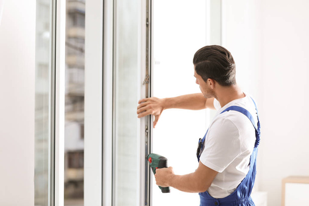 Construction worker repairing plastic window with screwdriver indoors - Foto, Bild