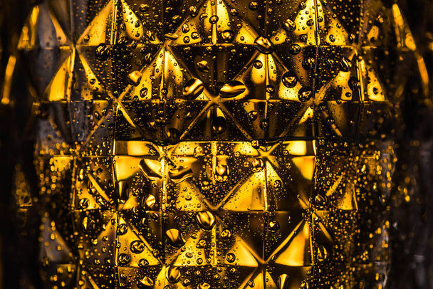 Nahaufnahme von geometrisch facettiertem Glas mit gelber Beleuchtung im Dunkeln - Foto, Bild