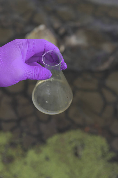 Eine Wasserprobe aus dem Fluss. Hand in Hand sammelt Wasser im Reagenzglas. ökologisches Konzept - Foto, Bild
