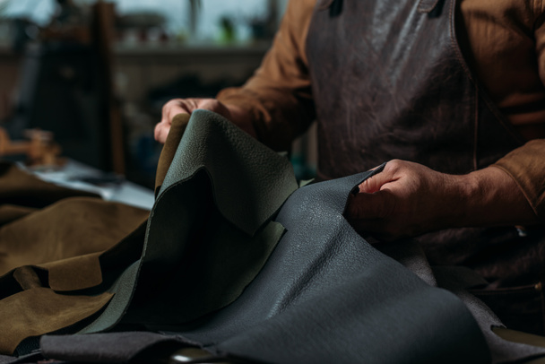partial view of shoemaker holding piece of genuine leather in workshop - Photo, Image