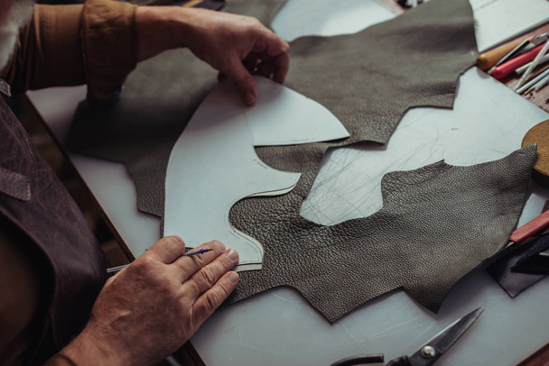 bijgesneden weergave van schoenmaker houvast stuk leer in de buurt van sjabloon in workshop - Foto, afbeelding