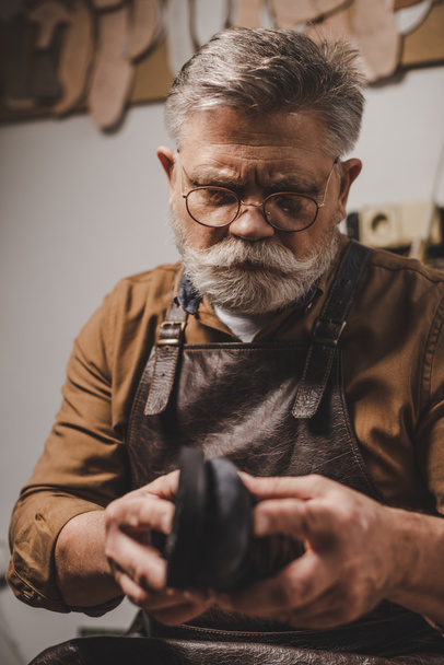 senior, bearded cobbler repairing shoe in workshop - Fotografie, Obrázek