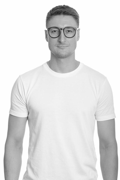 Studio shot of young handsome nerd man with eyeglasses isolated against white background in black and white - Foto, imagen