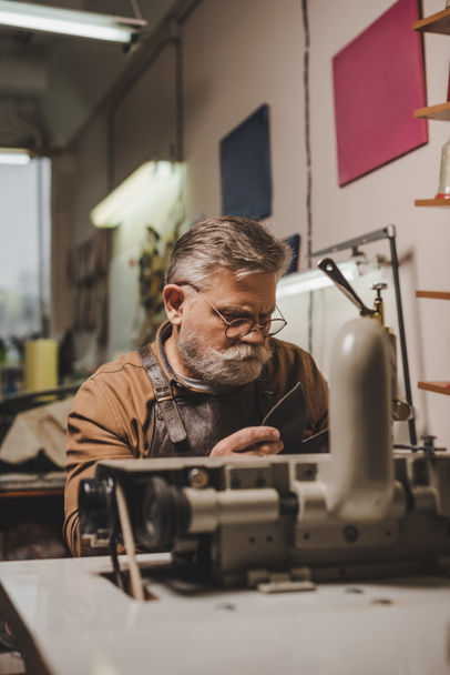 foco seletivo de couro de costura sapateiro sênior na máquina de costura na oficina
 - Foto, Imagem