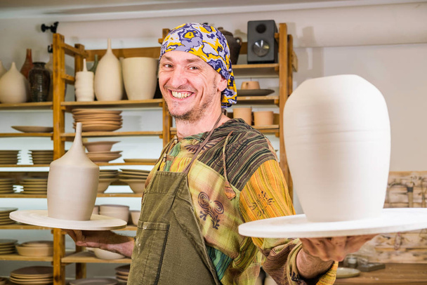Élégant maître potier tenant des produits d'art de la poterie dans son atelier. Faire concept de poterie
. - Photo, image