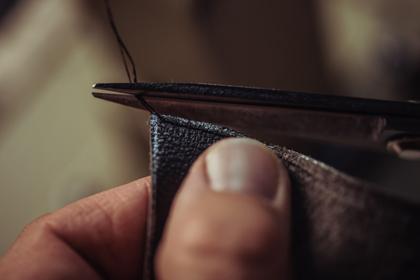 cropped view of cobbler cutting thread near piece of genuine leather - Photo, Image
