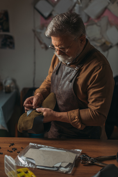 Oberschuster in Schürze hält Stück echtes Leder in Werkstatt - Foto, Bild