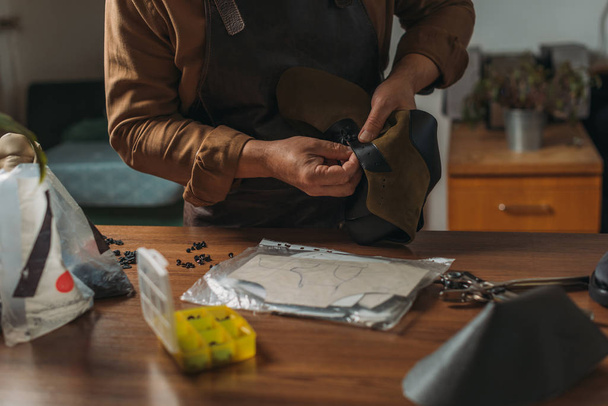 обрезанный вид сапожника, держащего кусок кожи возле стола с инструментами
 - Фото, изображение