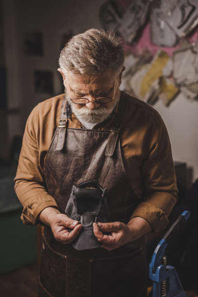 attentive, senior cobbler holding leather detail in workshop - Foto, Imagen