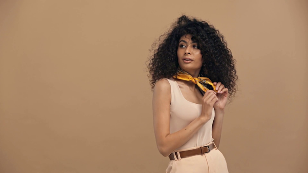 flirty bi-racial woman touching hair while posing isolated on beige - Felvétel, videó