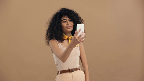 wesoły birasowy kobieta biorąc selfie izolowane na beżowy - Materiał filmowy, wideo