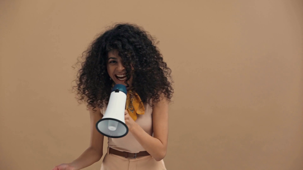 opgewonden bi-raciale vrouw spreken in megafoon geïsoleerd op beige - Video