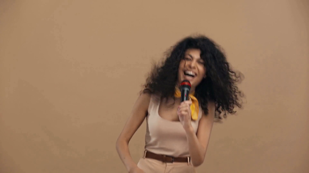 fröhliche bi-rassische Sängerin singt in Mikrofon isoliert auf beige - Filmmaterial, Video