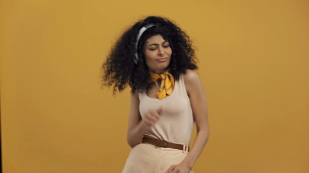 veselá bi-rasová žena tančí v bezdrátových sluchátkách izolovaných na tmavě žluté - Záběry, video