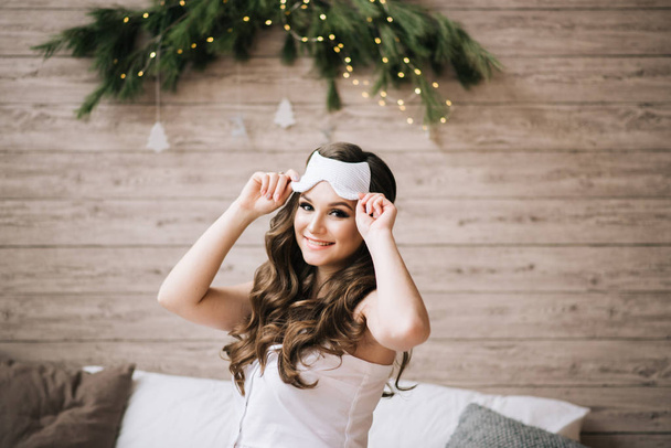 Close-up portrait of happy young woman  posing in morning.Smiling Woman with sleeping mask,top view.Attractive funny model white background.Sleep concept. - Fotó, kép