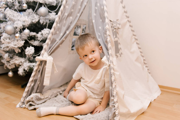 A small cute baby boy is sitting in the children's room in a ten - Photo, Image