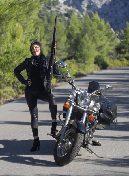 Una donna in giacca nera da motociclista con un fucile da carabina su una moto da elicottero in Grecia su una strada nel bosco in montagna
 - Foto, immagini