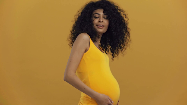 glücklich bi-rassische schwangere Frau berührt Bauch isoliert auf dunkelgelb - Filmmaterial, Video