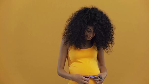 cheerful bi-racial pregnant woman measuring belly isolated on dark yellow - Metraje, vídeo