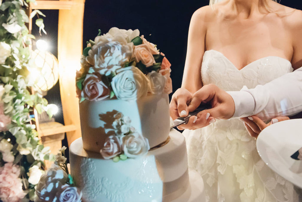 Sposi tagliare lussuosa torta bianca a quattro livelli con fiori
 - Foto, immagini