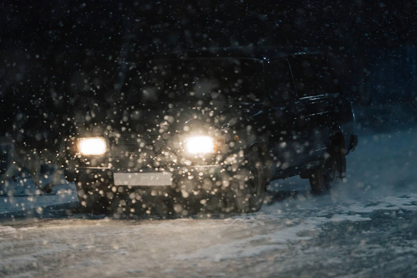 Keskittynyt tausta. Auton ajovalot tiellä raskaan lumen aikana
. - Valokuva, kuva